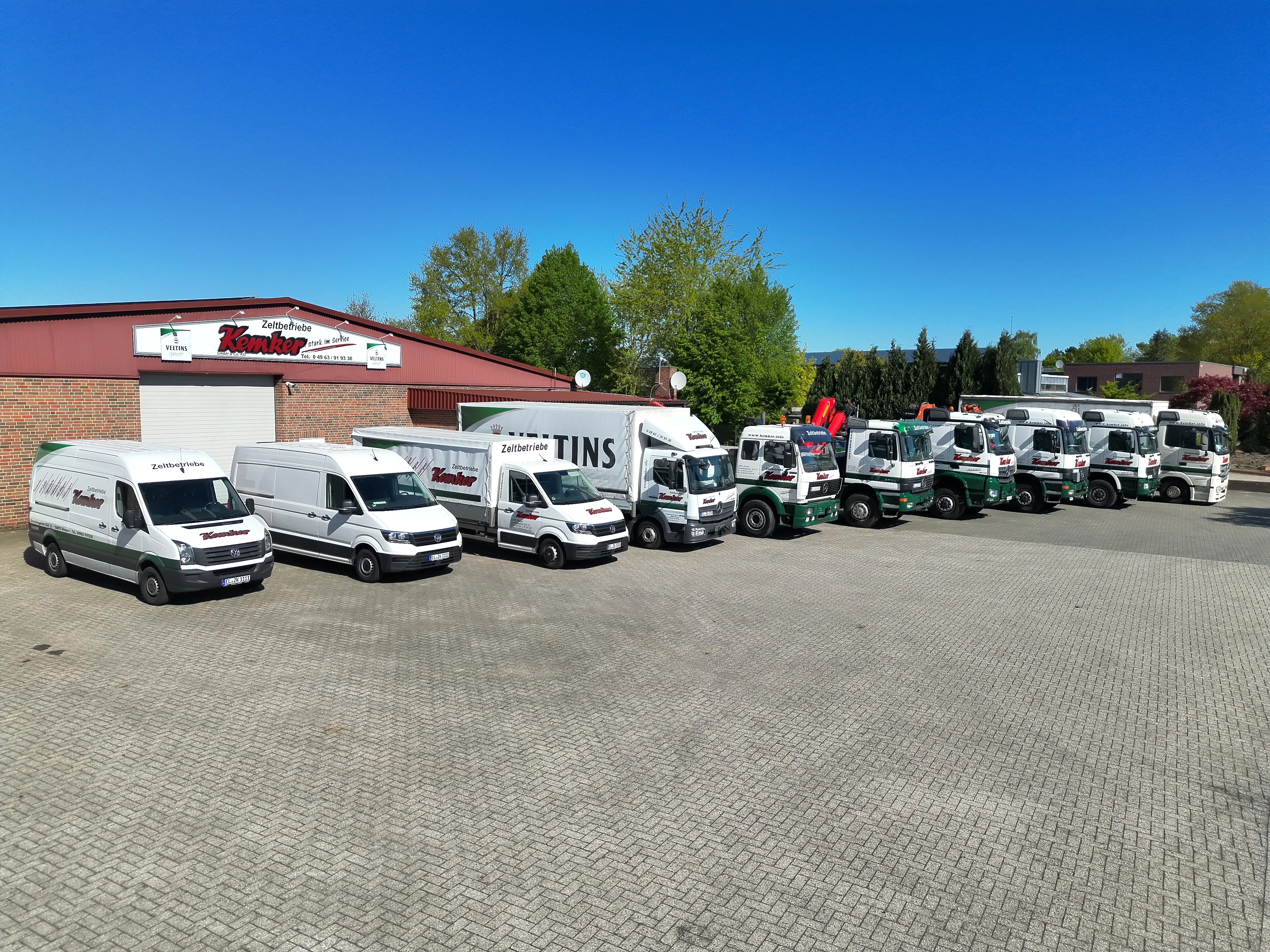 Fuhrpark von Kemker Zeltbetriebe: mehrere beschriftete Transporter und Lkw mit Kranfahrzeugen auf dem Betriebsgelände in Dörpen
